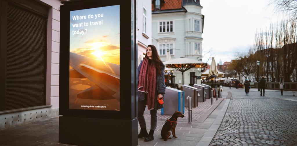 Woman looking at the electronic smart sign OOH advertising display in the city center, browsing the tourist locations offers thinking of traveling.