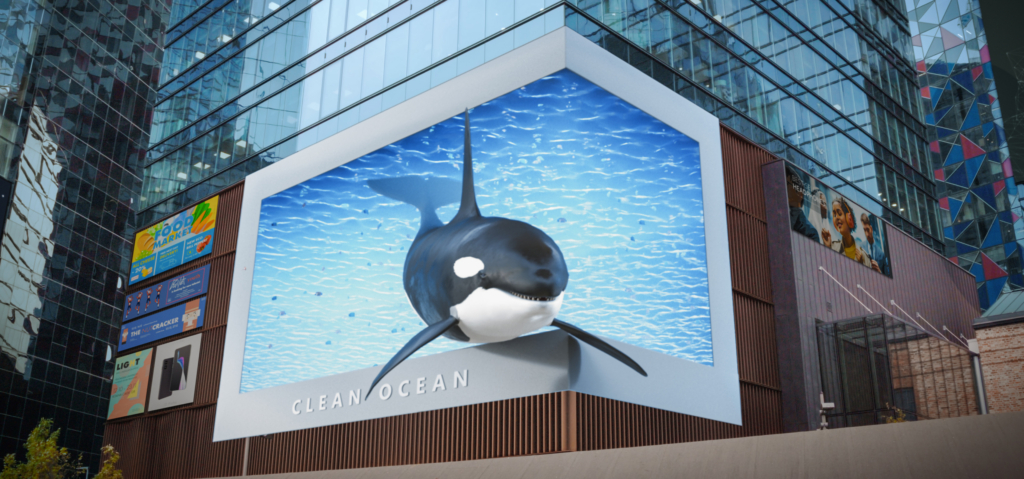 An anamorphic 3D digital OOH advertising display on a city building, showing a whale appearing to emerge from the digital screen. 